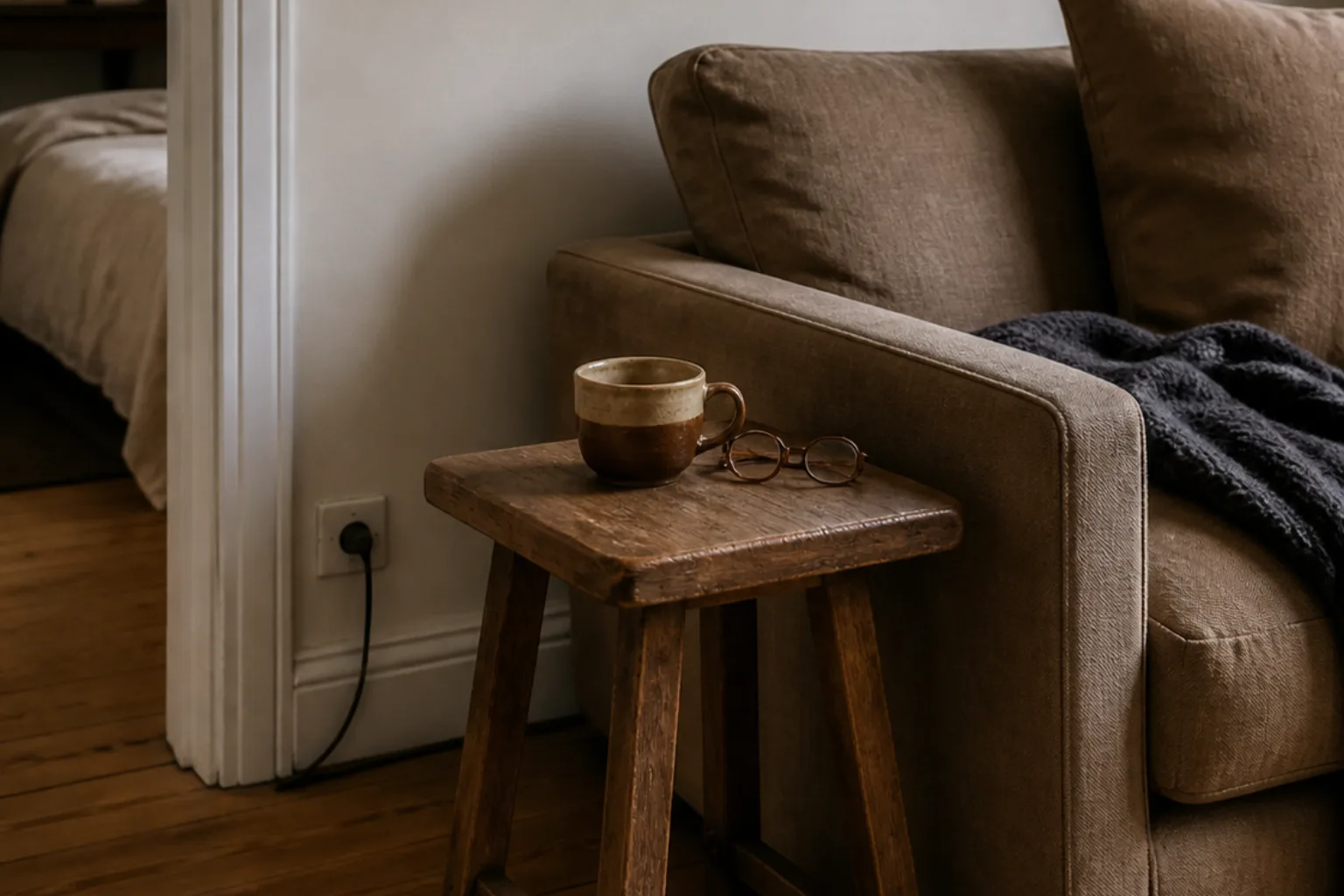 Worn wood stool used as a compact side table beside a rental sofa